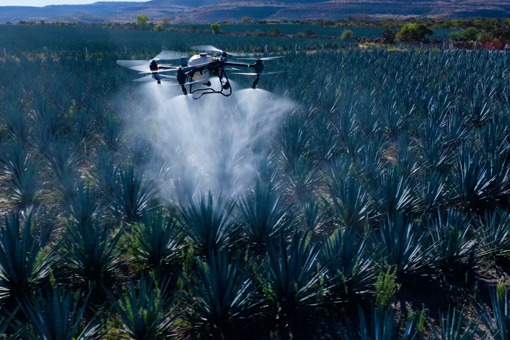 DJI AGRAS agricultural drone applying a liquid treatment over a commercial crop field.