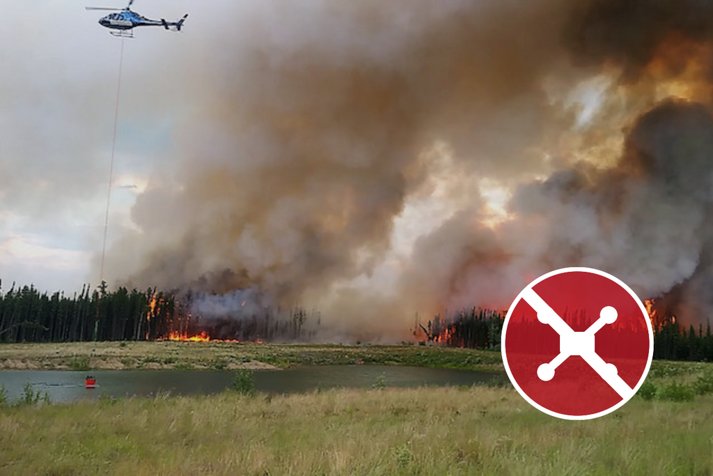 Firefighting helicopter operating over a Canadian wildfire with a no-drone safety symbol.